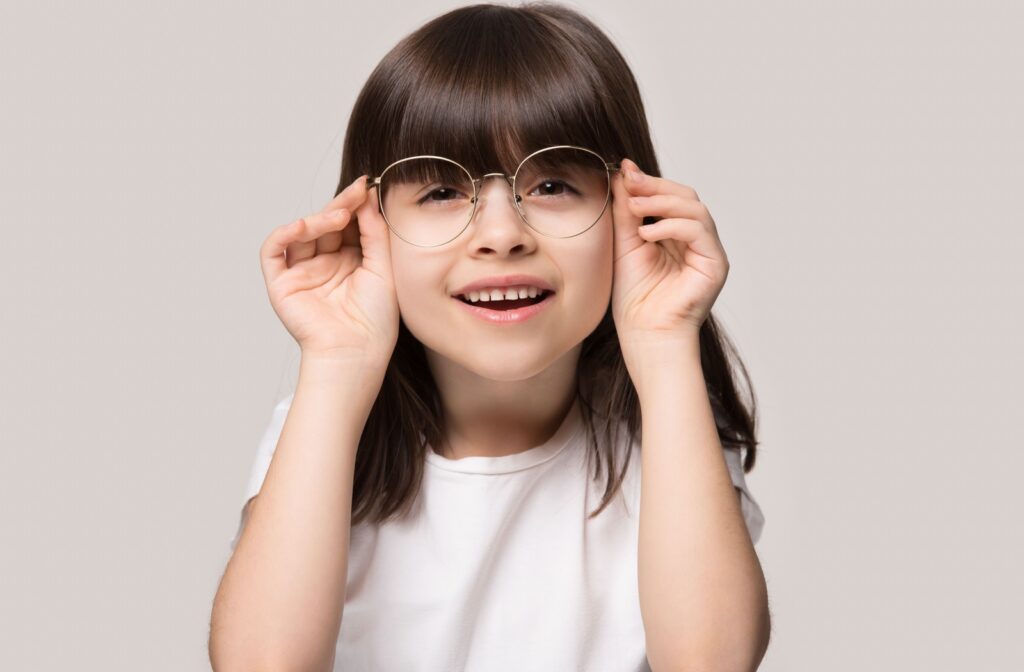 A young child curiously looks through her glasses lenses.