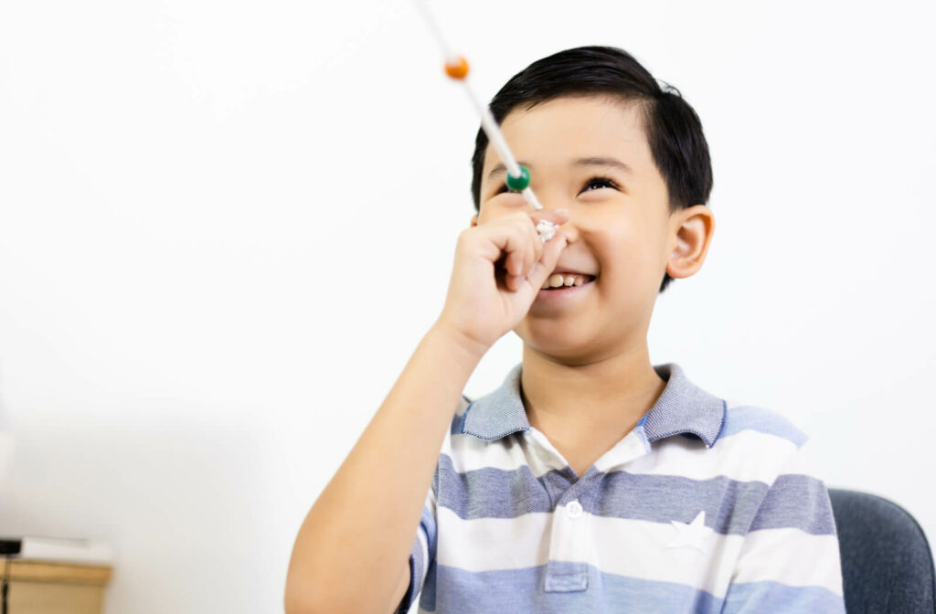 A young boy smiling performing a brock string exercise during vision therapy.