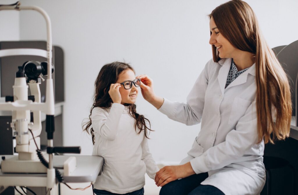 A little girl attends an eye exam. The eye doctor adjusts the glasses on the girl's face.